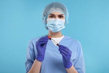Laboratory testing. Doctor with blood sample in tube on light blue background