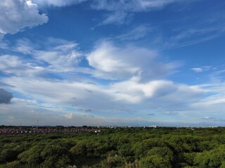 Aerial view of lush green field in a rural area under blue cloudy sky with buildings in background