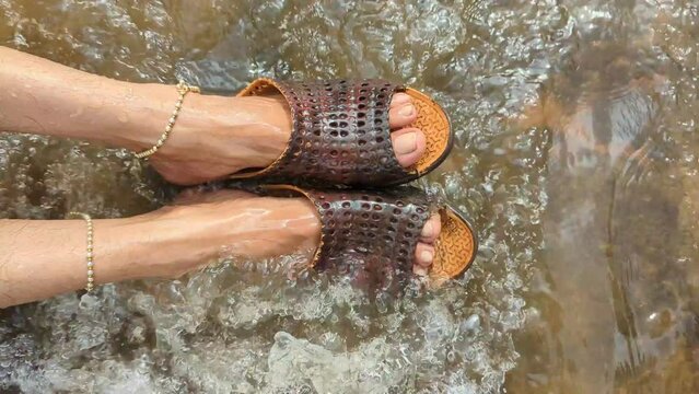 Closeup of water flowing over human feet wearing sandals with a strong stream
