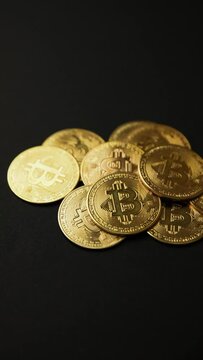 Close up of a pile of bitcoins golden coins on a black background, camera panning movement, vertical shot. Bullish BTC, cryptocurrency, 2p2 exchange and blockchain concept