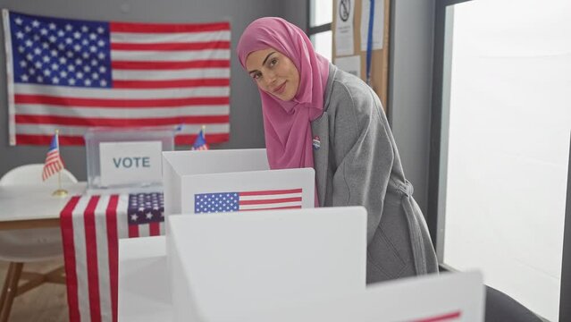 A smiling woman with a hijab and voter sticker participates in the american democratic process at a polling station with us flags.
