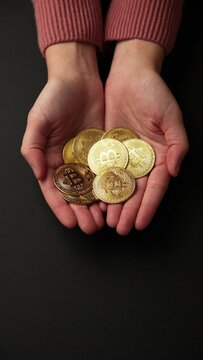 Hands showing a pile of bitcoins golden coins on a black background, vertical shot. Bullish BTC, cryptocurrency, 2p2 exchange and blockchain concept