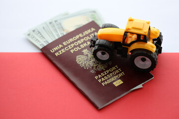 Red polish passport and yellow tractor on US money and smooth red and white flag of Poland close up