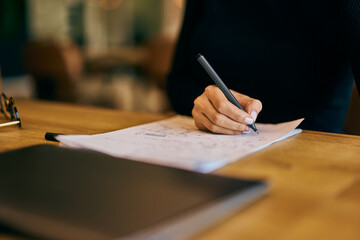 Close-up of a female holding a pen and making some notes on the paper, at the office.