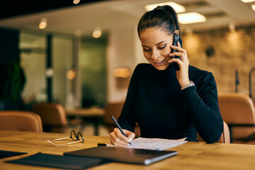 A smiling businesswoman working at the office, making a phone call.