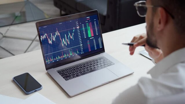 Investor using laptop looking at computer screen checking trade market data. Stock trader broker analyzing online trading cryptocurrency finance market crypto stockmarket data, over shoulder view.