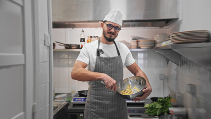 Male head chef prepare tasty fresh dish. Man cook meal restaurant kitchen. Young adult person work at cafe cuisine wear white hat. Guy make diet lunch food. Culinary worker job. Cookery staff uniform. - obrazy, fototapety, plakaty