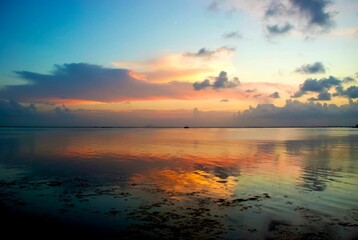 Scenic view of a boat sailing in a tranquil sea, reflecting the beautiful sunset