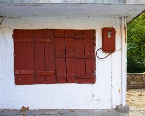 Wooden red window and an electric meter box on an old white wall.