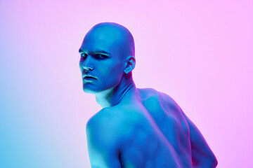 Relief back, Young bald man posing shirtless on gradient blue pink background in neon light. Muscular body. Concept of male beauty, body, youth, fitness, sport, health