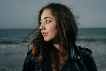 Portrait of young woman in leather jacket at the sea - 782971024
