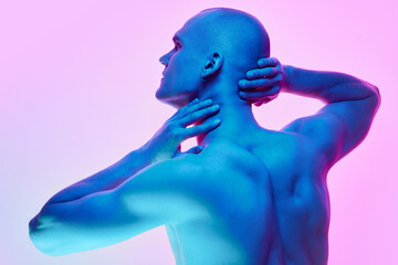 Relief back, Young bald man posing shirtless on gradient blue pink background in neon light. Muscular body. Concept of male beauty, body, youth, fitness, sport, health