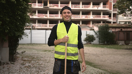 Street cleaner sweep leaves city road asphalt. Smile sweeper man portrait. Happy janitor clean sidewalk. Urban worker look at camera. Young adult guy work outdoor Person hold cleanup broom Outside job