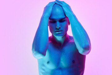Self-identity. Portrait of young man with bald head, posing shirtless on gradient blue pink background in neon light. Concept of male beauty, body, youth, fitness, sport, health