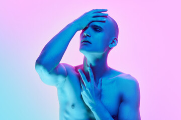 Self-identity. Portrait of young man with bald head, posing shirtless on gradient blue pink background in neon light. Concept of male beauty, body, youth, fitness, sport, health
