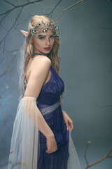 A young woman in a blue dress and veil, embodying a fairy princess in a studio setting.