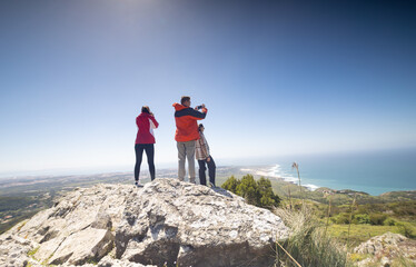 Three People Standing on Top of a Mountain Overlooking the Ocean
