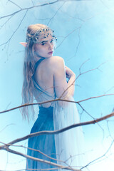 A young woman in a flowing blue dress stands gracefully in a tree, embodying a fairy princess in a fantasy world.