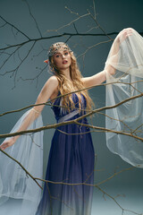 A young woman in a blue dress stands gracefully in front of a towering tree, embodying an ethereal fairy princess in a studio setting.