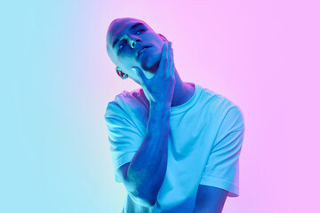 Handsome young man with bald head, shaved face and well-kept skin posing on gradient blue pink background in neon light. Concept of male beauty, body, youth, fitness, sport, health