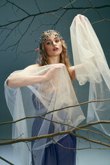 A young woman in a beautiful blue dress and a flowing white veil, embodying the essence of a fairy or fantasy elf princess in a studio setting.