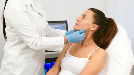 A female cosmetologist-dermatologist talks to a client sitting in a comfortable salon chair....