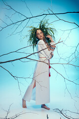 A young mavka in a white dress gracefully holds a delicate branch in a whimsical studio setting.
