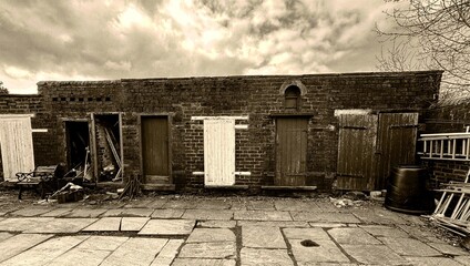 Victorian brick outhouses, with multiple wooden doors, some of which appear damaged or boarded up near, Cliff Hollins Lane, Oakenshaw, Bradford, UK,  (Sepia Version)