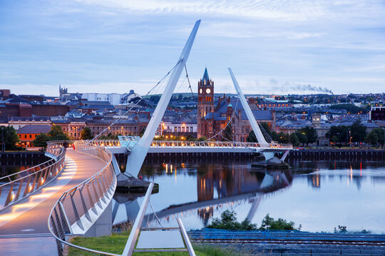 Derry, Ireland. Illuminated Peace bridge in Derry Londonderry, City of Culture, in Northern Ireland with city center at the background. Night cloudy sky with reflection in the river at the dusk