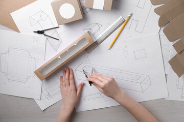 Woman creating packaging design at light wooden table, top view