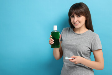 Young woman with mouthwash and toothbrush on light blue background, space for text