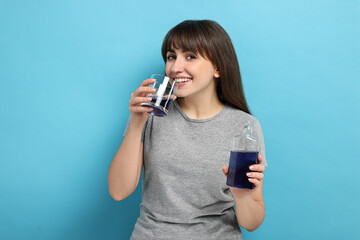 Young woman using mouthwash on light blue background