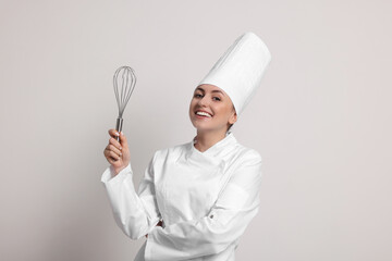 Happy professional confectioner in uniform holding whisk on light grey background