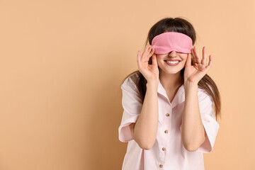 Woman in pyjama and sleep mask on beige background, space for text