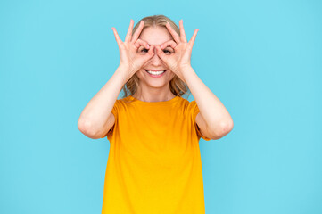 Happy woman making finger glasses at eyes on blue background.