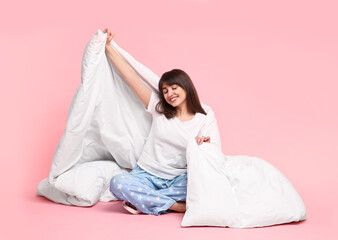 Happy woman in pyjama wrapped in blanket on pink background