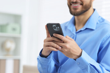 Young man using smartphone in office, closeup. Space for text
