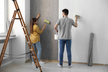 Woman and man hanging wallpaper in room