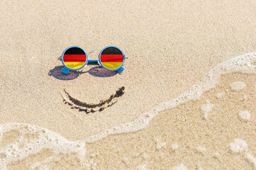 Fototapeta na wymiar A painted smile on the sand and sunglasses with the flag of the Germany.