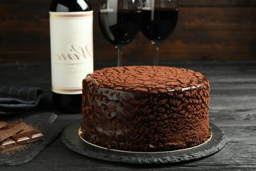 Delicious truffle cake, chocolate pieces and red wine on black wooden table