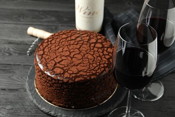 Delicious chocolate truffle cake, red wine and corkscrew on black wooden table
