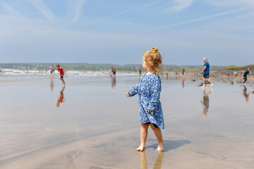Little cute toddler girl at the Ballybunion surfer beach, having fun on with playing on west coast of Ireland. Happy child enjoying Irish summer and sunny day with family.