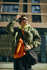 Stylish guy, student dressed oversized neon, merging urban chic with youthful exuberance posing against city skyline. Concept of street fashion, urban style, modern lifestyle, gen Z, self-expression.