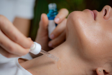 Cosmetician applying hyaluronic acid serum on woman's neck for targeted anti-aging benefits and...