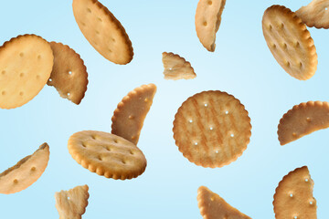 Tasty dry crackers falling on light blue background