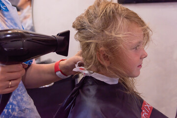The stylist makes a fashionable beautiful hairstyle for the child