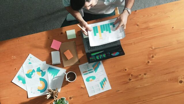 Top aerial view of manager working on laptop while looking at data analysis. Leader compare financial statistic graph while making decision at meeting table with document scatter around. Convocation.