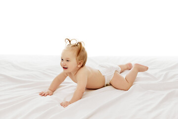 Happy, smiling, little redhead girl, toddler in diaper lying on belly on bed and laughing isolated on white background. Happiness. Concept of childhood, care, health, well-being, parenthood