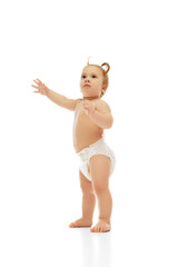 Curious little baby girl, toddler, kid in diaper, with two ponytails standing with raised arm isolated on white background. Exploring world. Concept of childhood, care, health, well-being, parenthood
