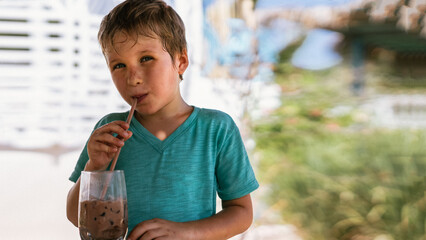 Happy childhood. Boy drinking chocolate tea with ice in hot summer day time. Cute lover of sweets...